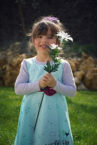 Portrait of smiling girl holding flower while standing in lawn