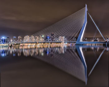 Illuminated erasmusbrug with reflection in nieuwe maas against sky at night