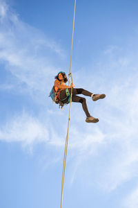 Low angle view of man climbing rope against sky