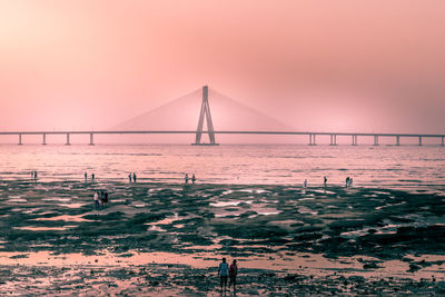 Suspension bridge over sea against sky during sunset