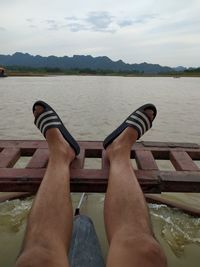 Low section of man relaxing on lake against sky