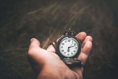 Cropped hand holding pocket watch outdoors