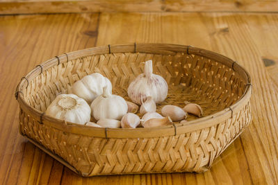 Dried garlic is placed in a wicker basket placed on a wooden floor.