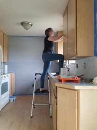 Woman on standing on ladder in kitchen at home