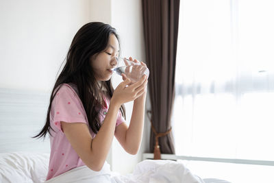 Side view of beautiful woman drinking from bed