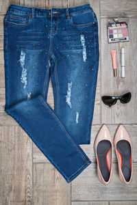 Flat lay of jeans with make-up and personal accessories on wooden floor