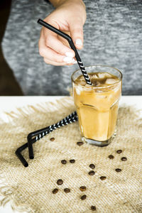 Close-up of hand holding drinking straw in cold coffee on table