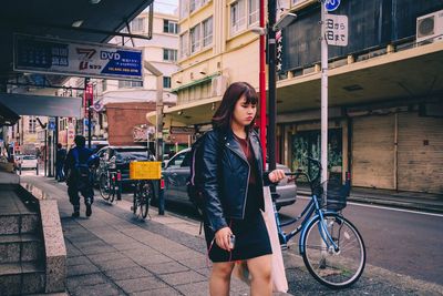 Woman with bicycle standing on street in city