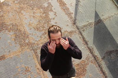 High angle view of man touching eyes while standing outdoors