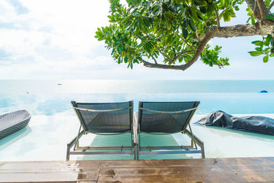 Deck chairs by swimming pool against sky