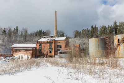 Snow covered field by building against sky