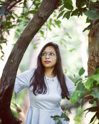 Portrait of beautiful young woman standing by tree trunk