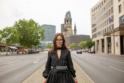 Portrait of young woman standing on road in city