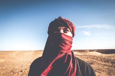 Portrait of woman standing on sand at field against clear sky