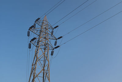 Low angle view of electricity pylon against clear blue sky