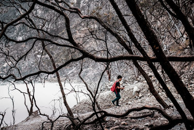 Full length side view of boy with red backpack walking in forest