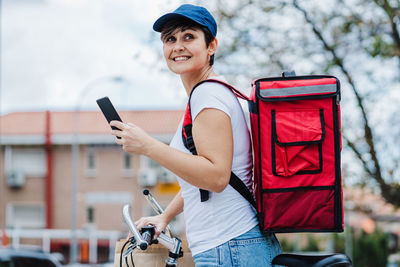 Woman with backpack delivering food on  bike, checking order with smart phone. delivery service