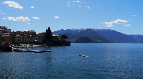 Sailboats in sea by buildings against sky