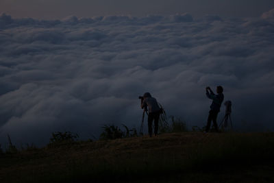 Silhouette friends photographing through camera while standing on field at dusk