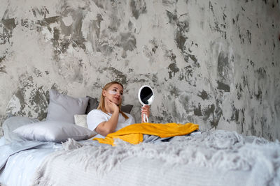 Young woman admires herself in mirror while in bed