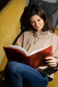 High angle view of woman reading book while lying on sofa