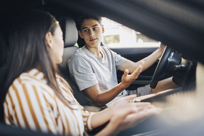 Young man getting driving lessons from mother while sitting in car