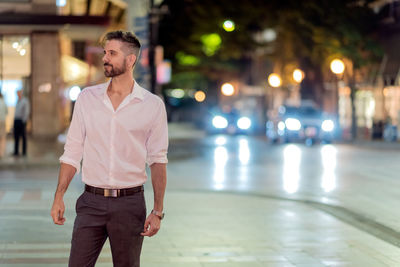 Businessman standing on sidewalk in illuminated city at night