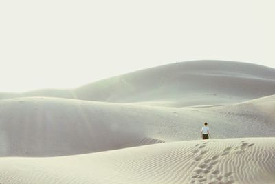 Rear view of man on sand dune in desert against sky