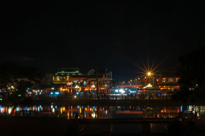 Illuminated buildings by river against sky at night