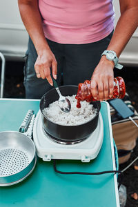 Close up of female hands putting tomato sauce to rice dish. woman cooking meal on electric stove