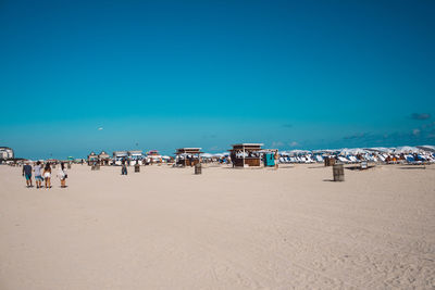 People at beach against clear blue sky