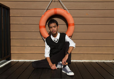 Portrait of young man sitting on wooden wall