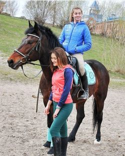 Full length portrait of happy woman riding horse on field