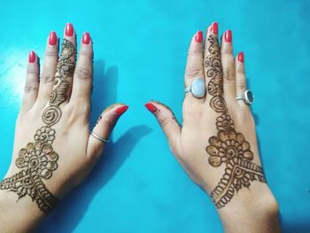 Cropped hands of woman showing henna tattoo at blue table