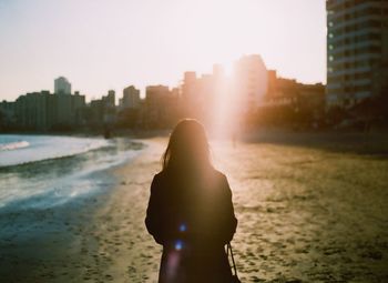 Rear view of woman walking on shore at beach in city