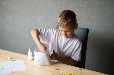 The boy cuts out details from paper. glue the parts together with glue.