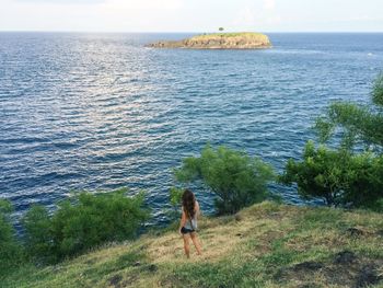 Rear view of woman standing on field by sea