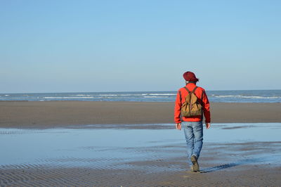 Rear view of man walking on beach against clear sky