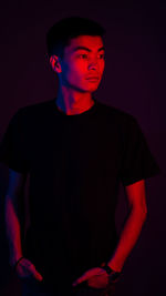 Portrait of young man standing against black background