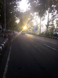 Road by trees against sky during sunset