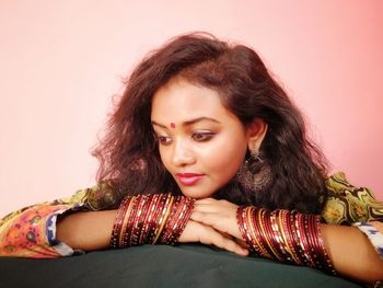 Beautiful young woman wearing bangles leaning against pink wall