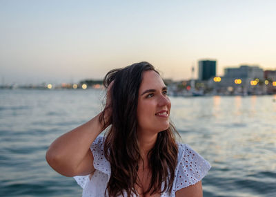 Portrait of pretty girl sitting on waterfront in city by sea during evening hours