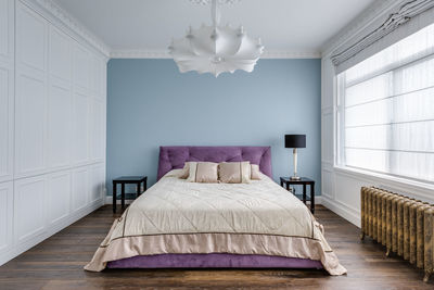 A large purple bed in a blue room near a large window. in the foreground is a glass partition