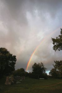 Rainbow over field against cloudy sky