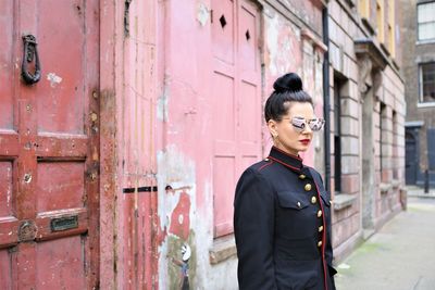 Woman wearing sunglasses while standing against wall in city