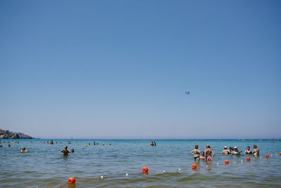 People on beach against clear blue sky