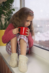 Cute girl drinking hot chocolate sitting by window