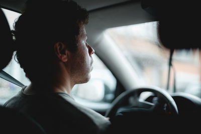 Young handsome caucasian guy looks behind the road while driving a car on a rainy day