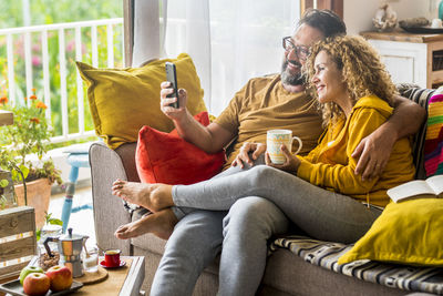 Smiling couple taking selfie through smart phone sitting on sofa