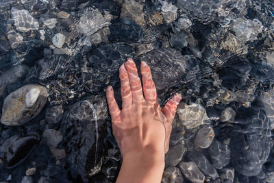 Cropped hand touching pebbles in river